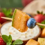 Colorful rainbow fruit skewers served with honey yogurt dip.