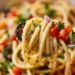 Colorful spaghetti salad with fresh vegetables and dressing served in a bowl.